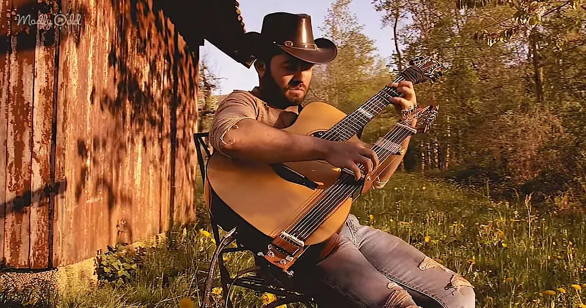 A man in a cowboy hat plays an acoustic guitar outdoors, surrounded by nature.