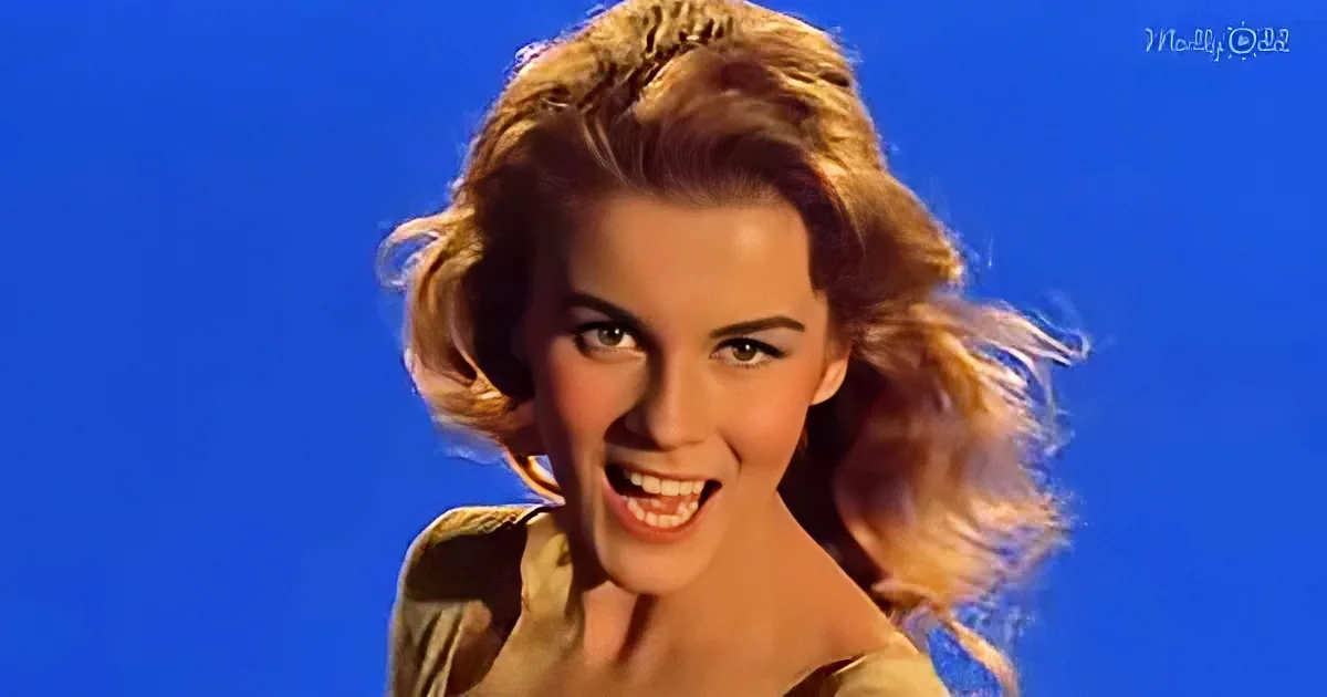 Blonde woman with a bright smile, wearing a light-colored top, against a vibrant blue background.