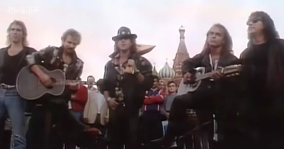 A group of musicians perform on stage, with a distinctive architectural backdrop featuring domes.