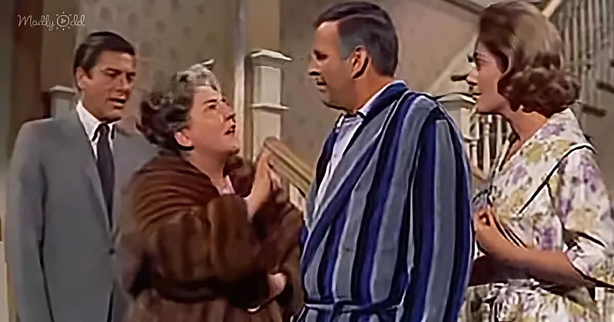 A woman in a brown coat is holding a book, seemingly in a heated discussion with a man in a striped robe.
