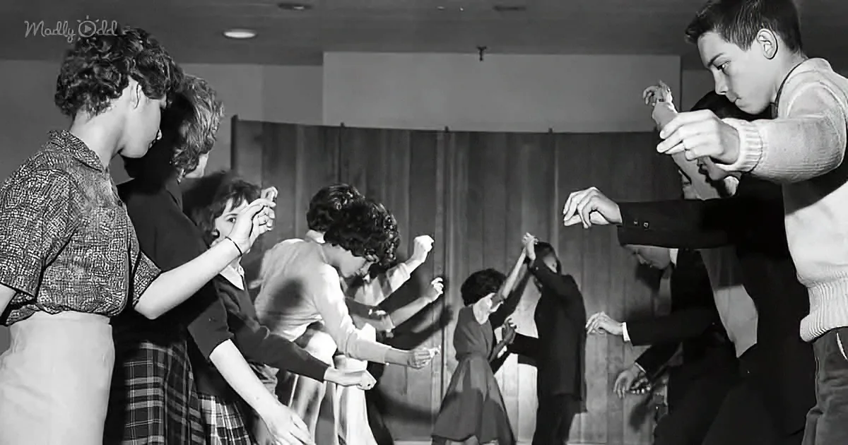 A group of people, mostly women, are dancing in a room, with one man leading the dance.
