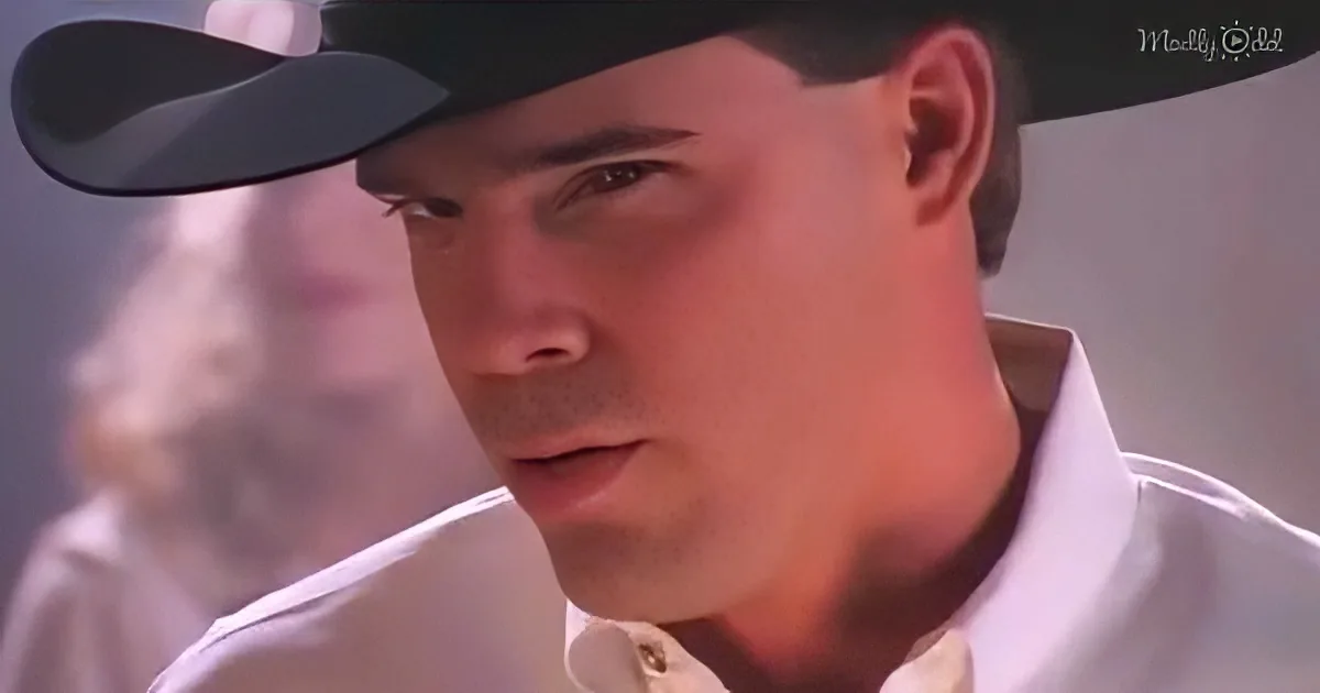 A man wearing a white shirt and a black cap, looking to the side with a serious expression.