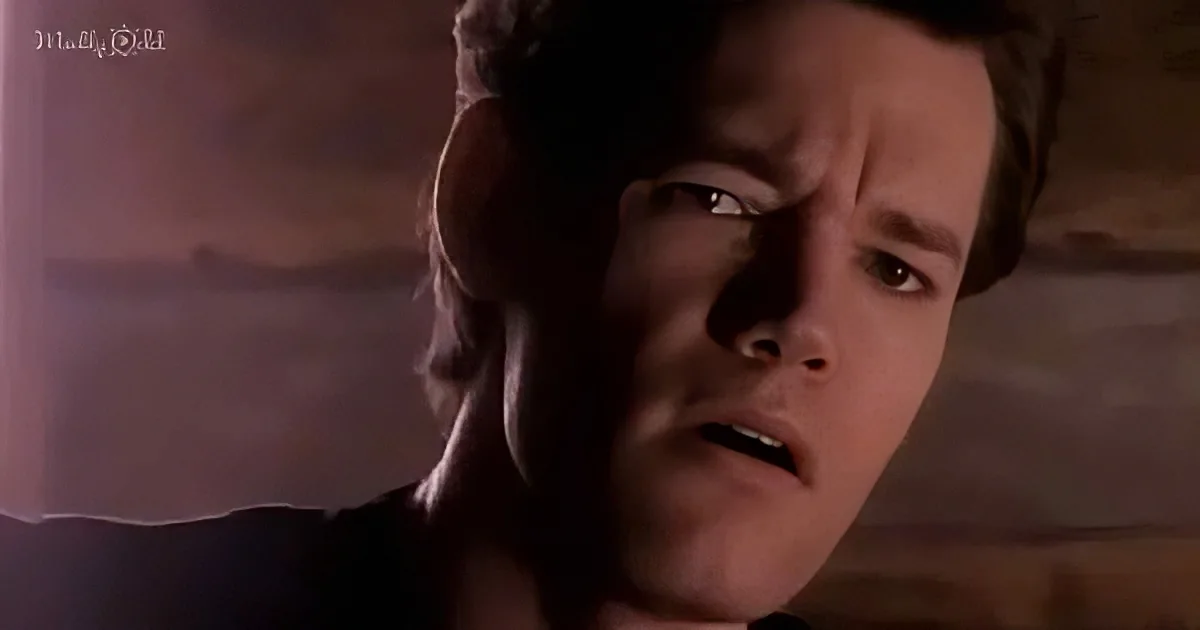 A man with a concerned expression, looking to the side, in a dimly lit setting.
