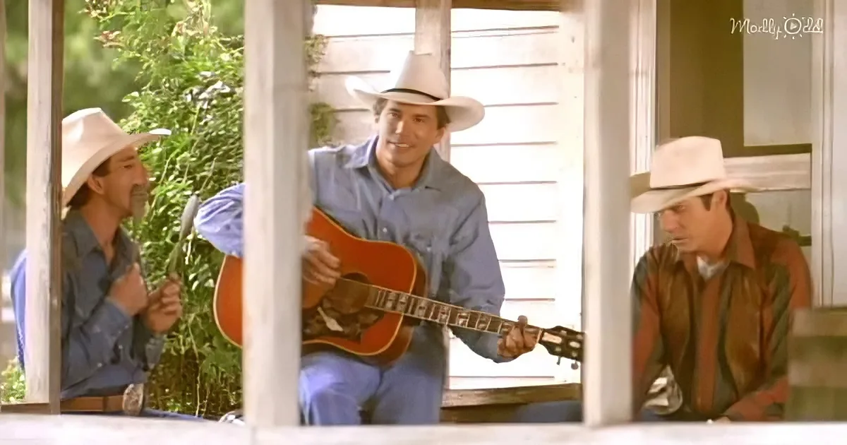 A man in a cowboy hat plays guitar on a porch, surrounded by two other men in similar attire.