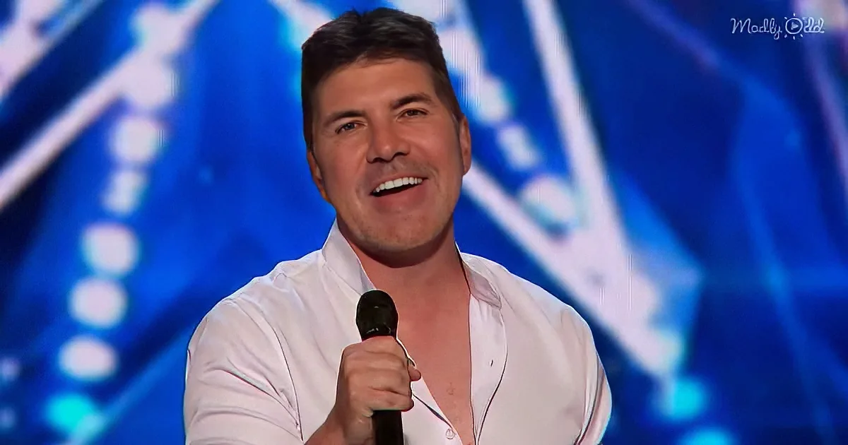 A man in a white shirt holds a microphone, smiling, with a blue background.