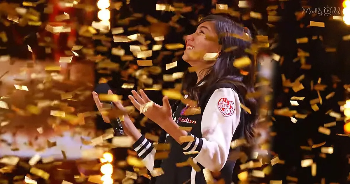 A person in a varsity jacket claps amidst falling golden confetti, smiling.