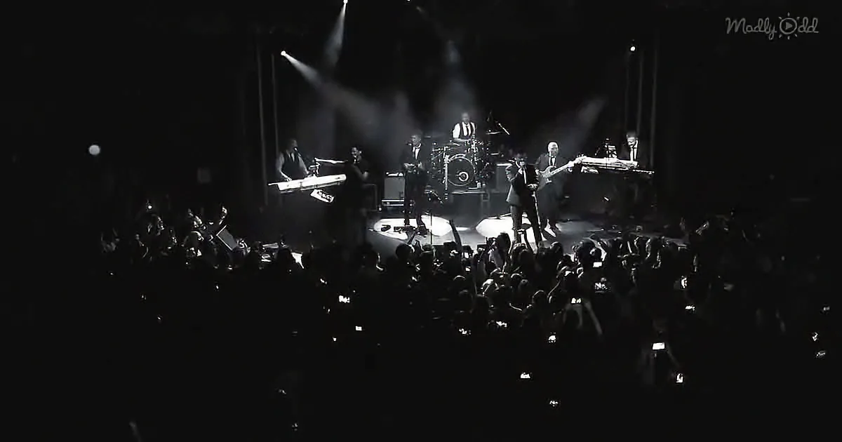 A band performs on stage under spotlights, surrounded by an energetic crowd.
