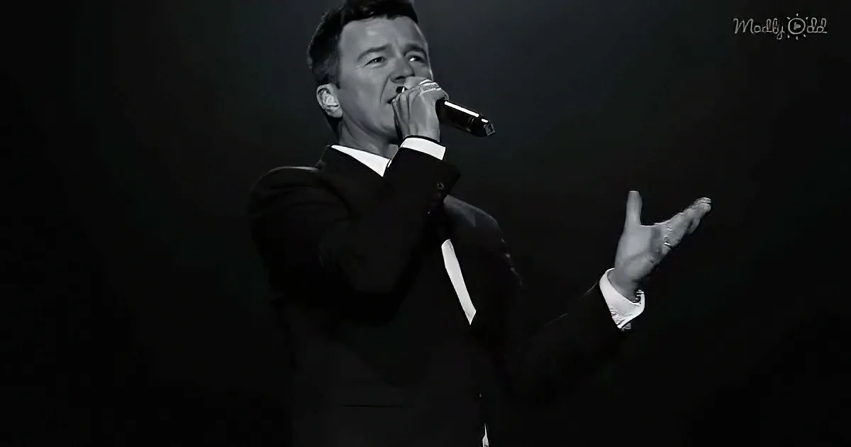 A man in a suit sings into a microphone, gesturing with his hand.