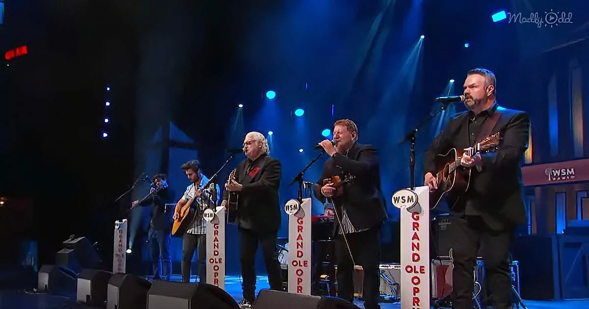 Musicians performing on stage at the Grand Ole Opry with microphones and instruments.