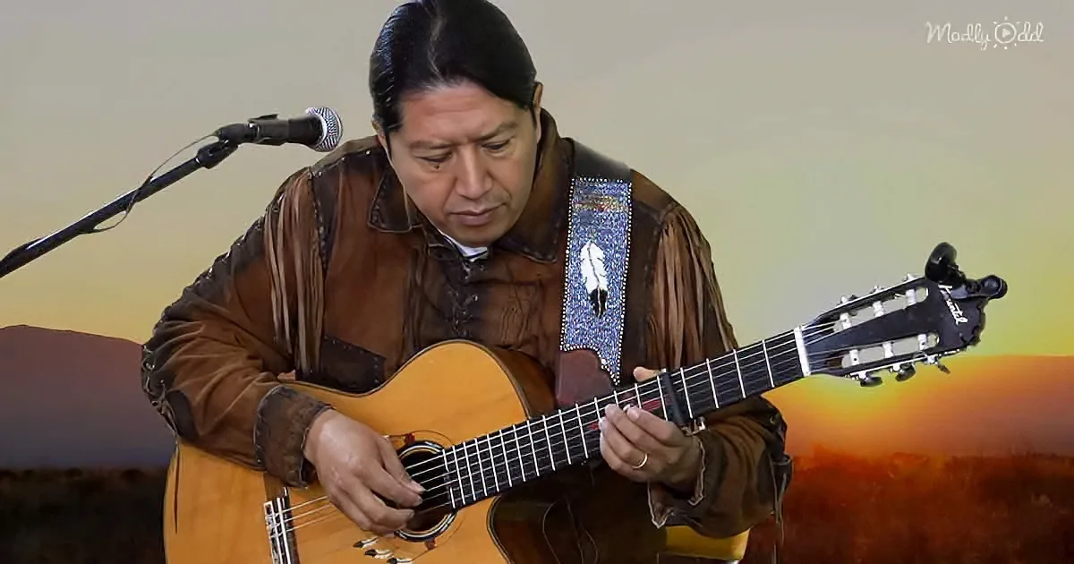 A man in a brown leather outfit plays a guitar with a microphone and a scenic background.