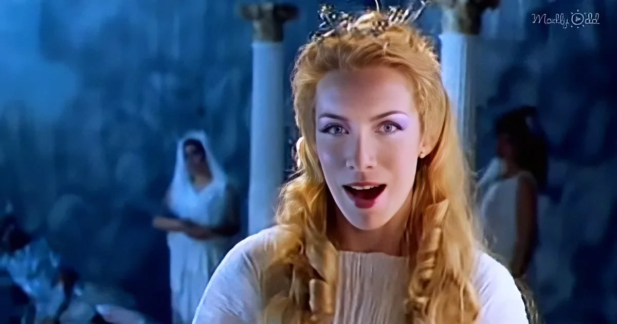 A woman with long blonde hair and a crown, wearing a white dress, appears surprised or shocked.