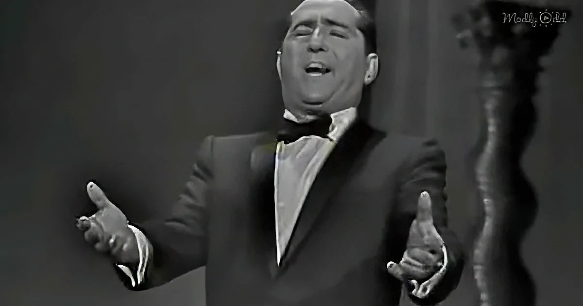 A man in a tuxedo sings passionately with outstretched arms, captured in a black-and-white image.
