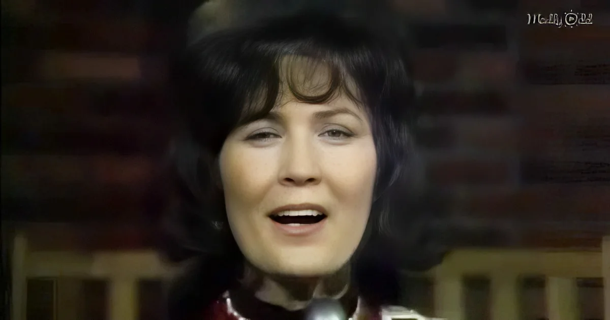 A person with dark hair and bangs, wearing a red top, is singing with their mouth open.