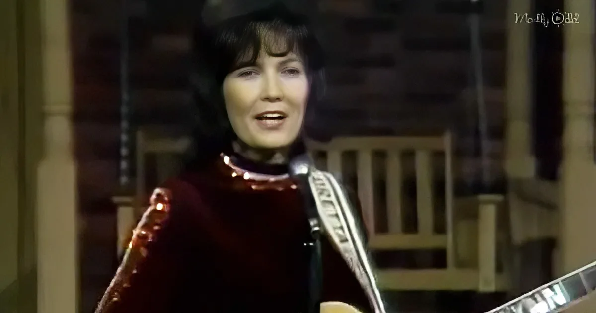 A woman in a red outfit and hat is singing while holding a guitar, with a microphone in front of her.