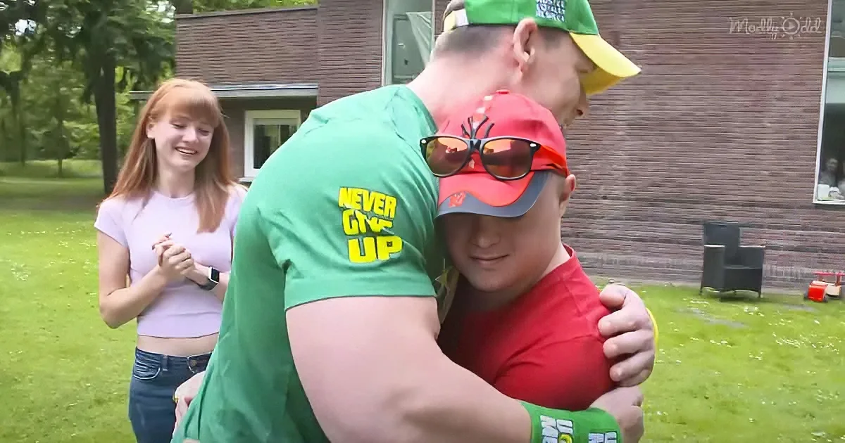 A man in a green shirt hugs another man wearing a red cap and sunglasses, while a woman in a pink top looks on.