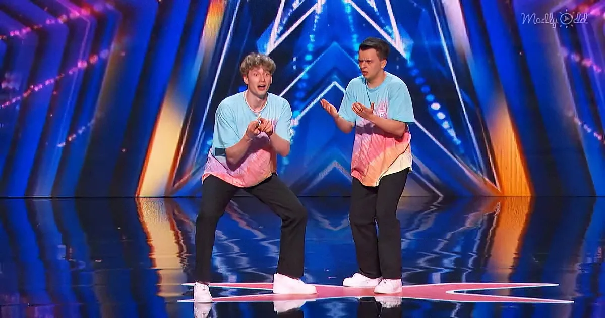 Two men in matching shirts perform on a brightly lit stage with dynamic background.