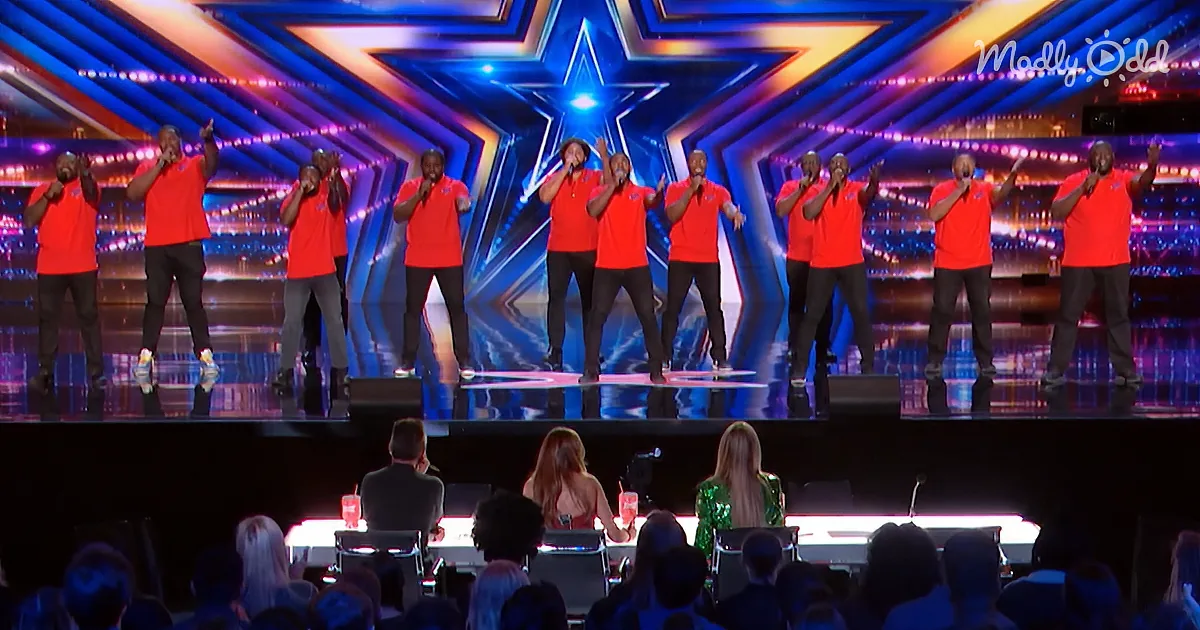 A group of men in red shirts perform on stage with a star backdrop, while judges and audience members watch.