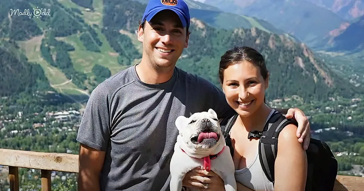 A couple and their white bulldog smile with a scenic mountain backdrop.