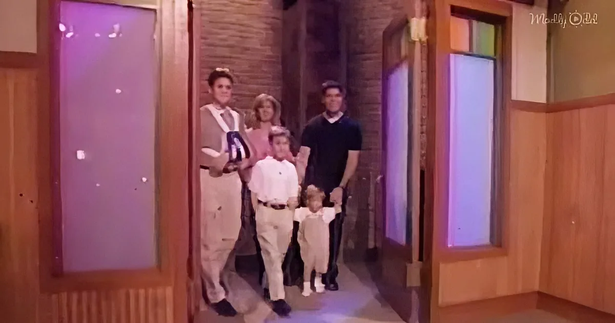 A family of five stands together in a hallway, dressed in formal attire, with a child in the center.