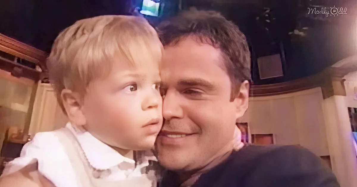 A man holds a young child, both smiling warmly in a cozy indoor setting.