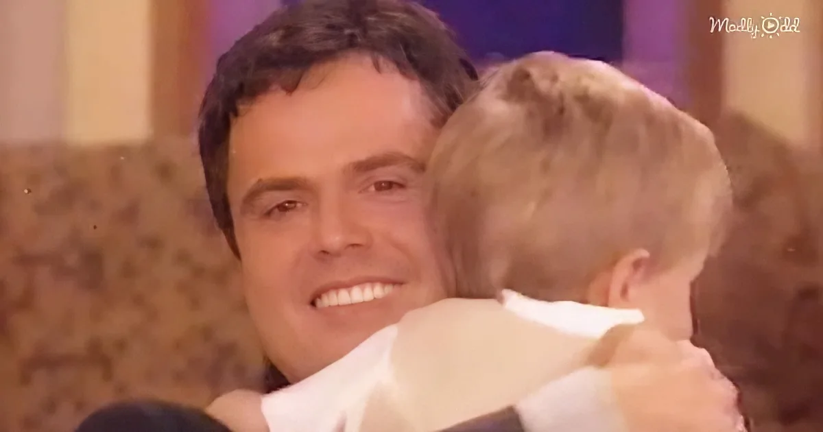 A man in a suit smiles warmly while embracing a child, both appearing happy and affectionate.