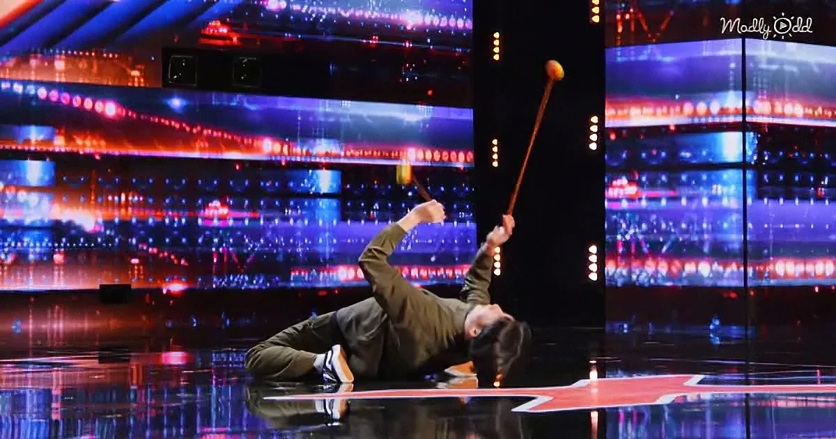A performer lies on stage, balancing a stick with a ball on it, surrounded by vibrant stage lights.