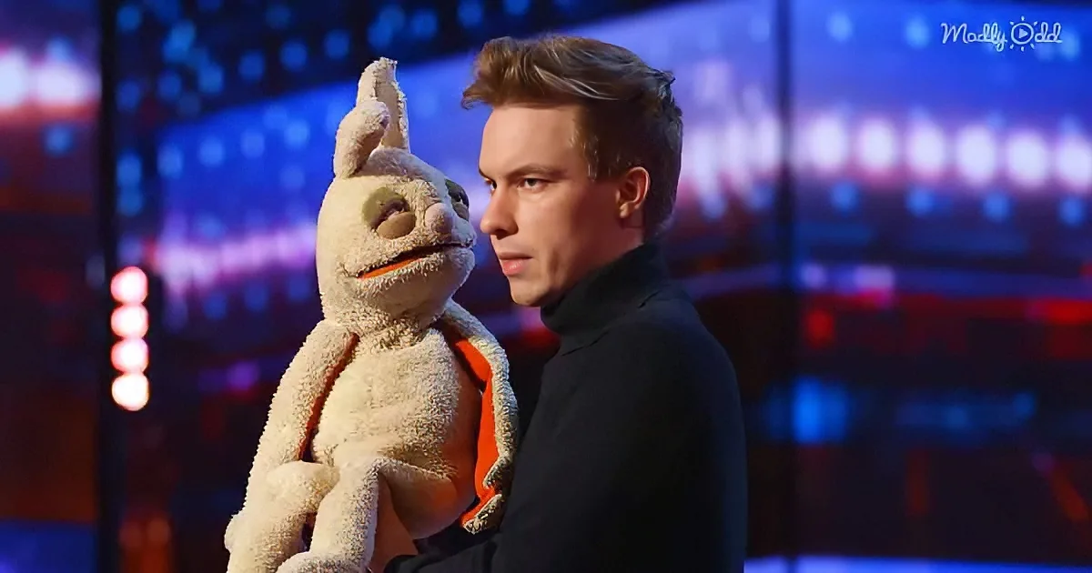 A man holds a plush rabbit puppet on a stage with colorful lights in the background.