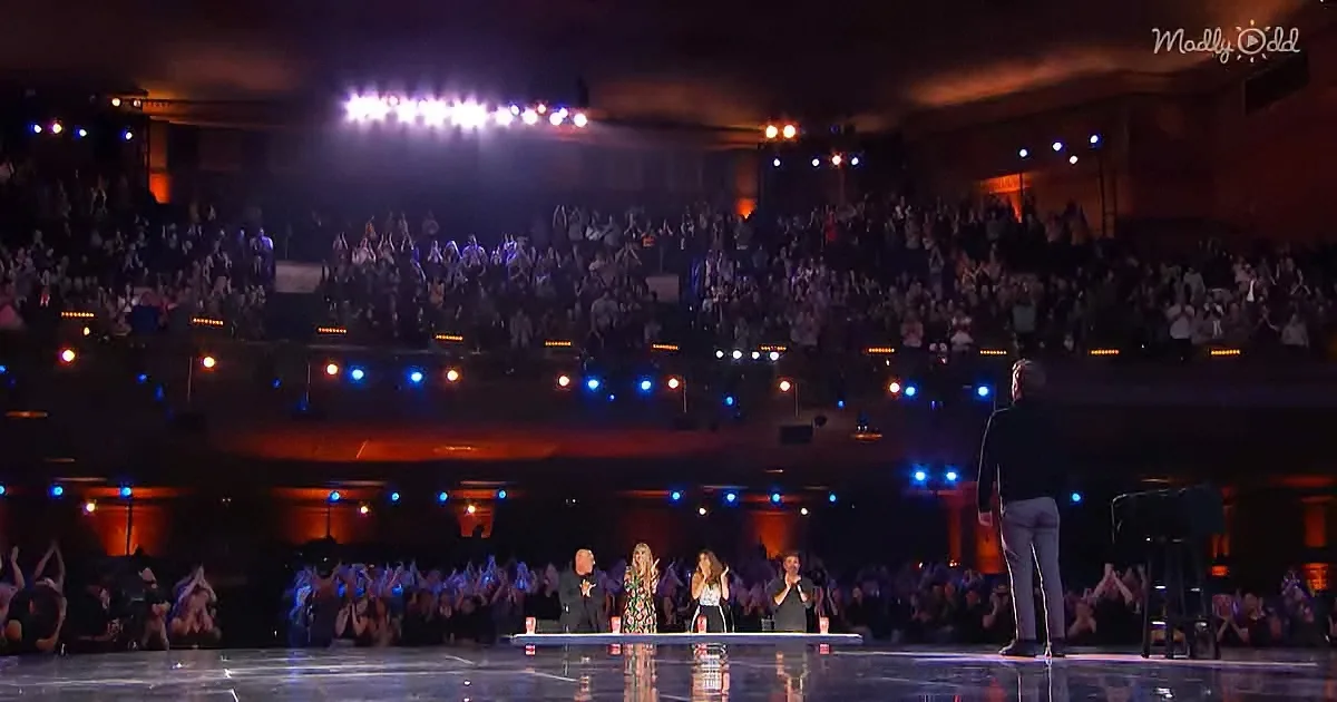 A man stands on stage facing judges and an audience, with bright lights illuminating the scene.