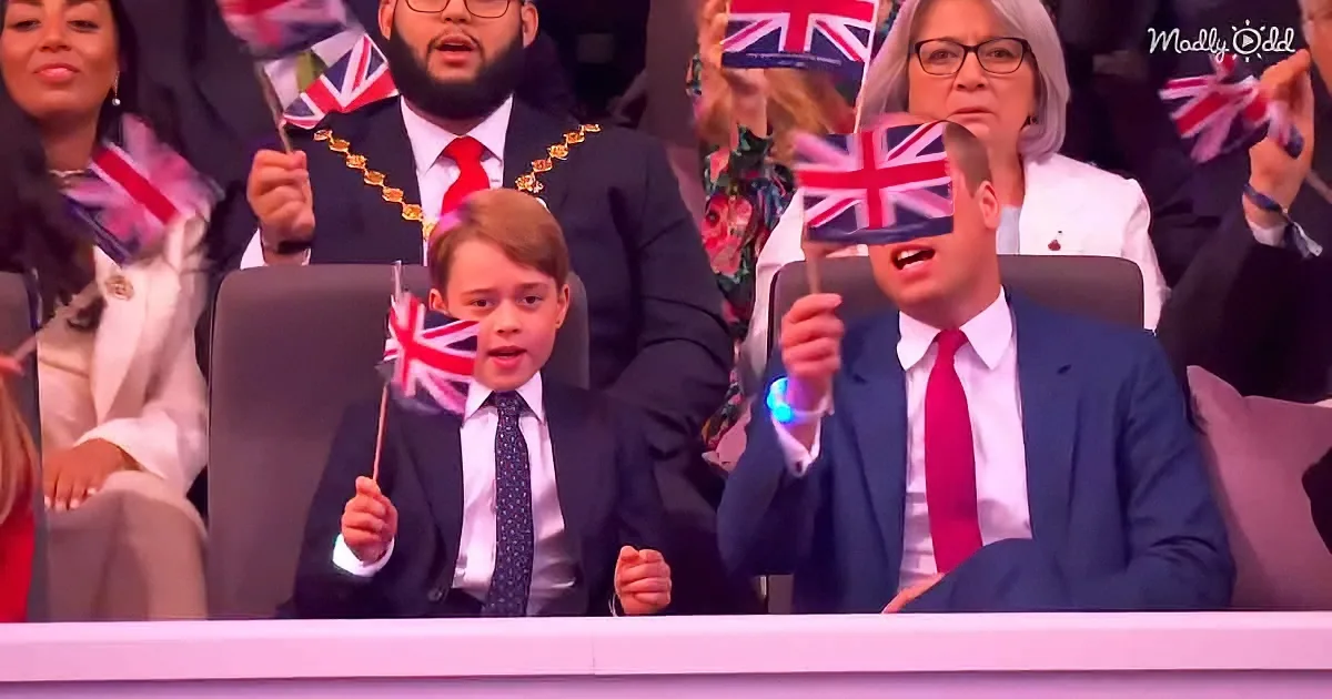 Prince George holds a Union Jack flag, seated next to a man in a blue suit, both in a formal setting with other attendees.