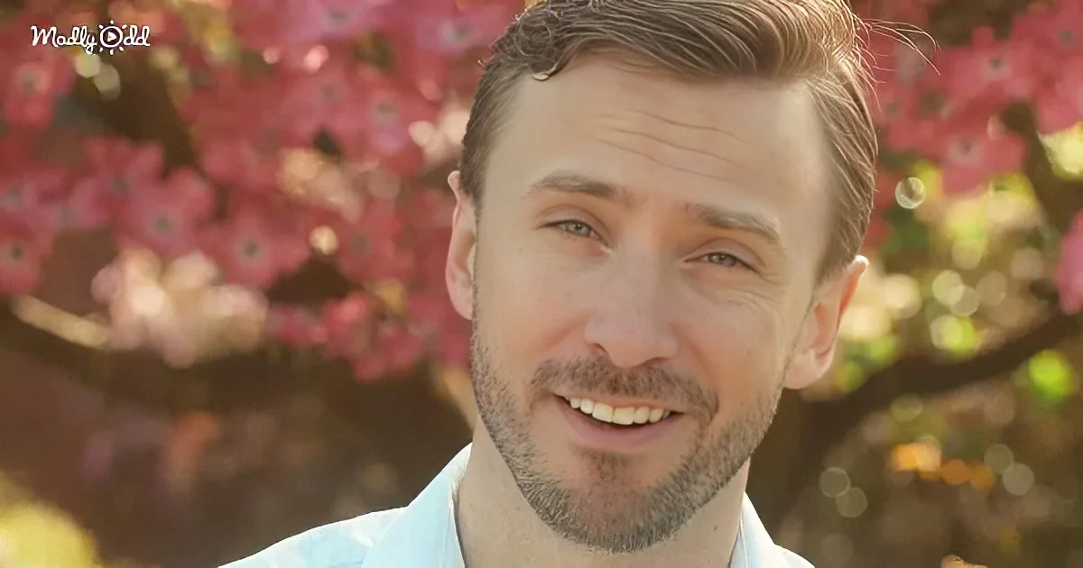 A man with short brown hair and a beard smiles in front of a blurred background of pink flowers.