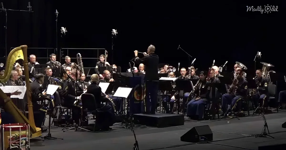 Conductor leads a military band in uniform on stage with instruments and sheet music.