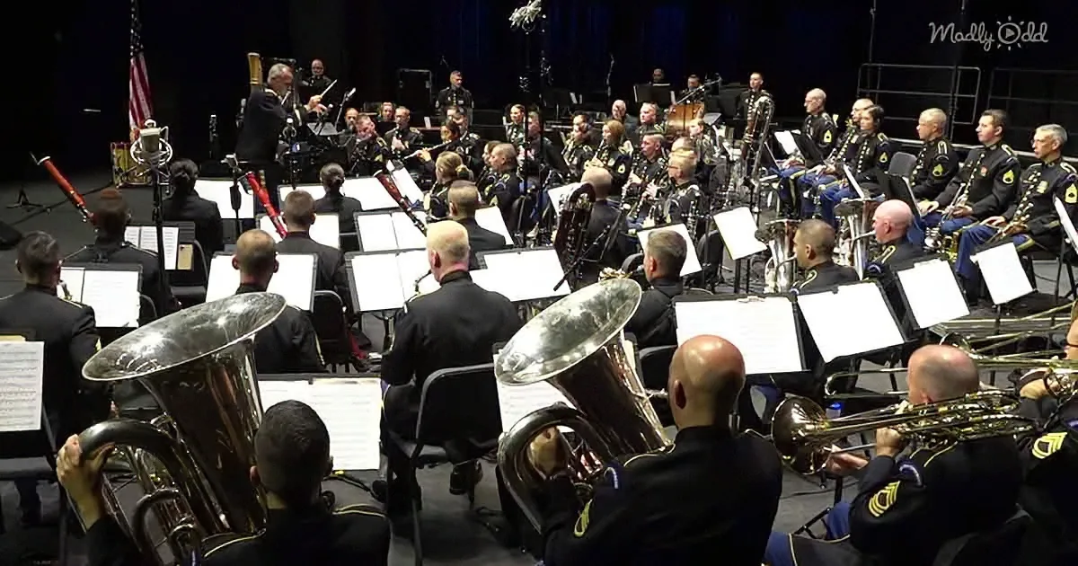A military band in uniform plays brass and woodwind instruments on stage with sheet music.