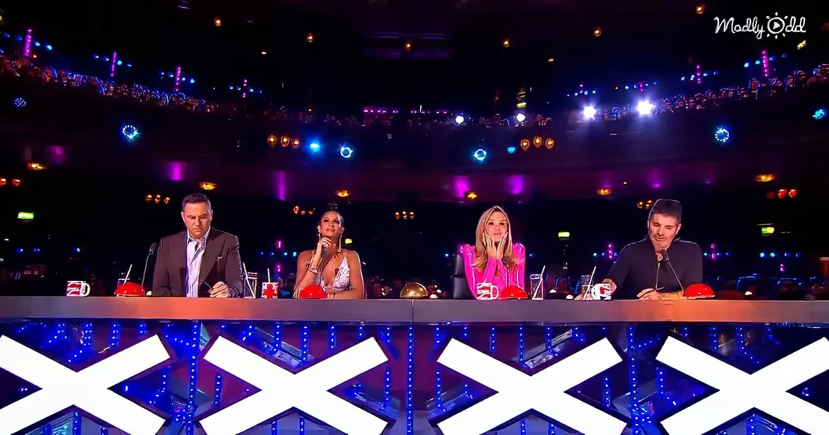 Judges sit at a table with mugs, surrounded by a colorful, illuminated audience in a large venue.