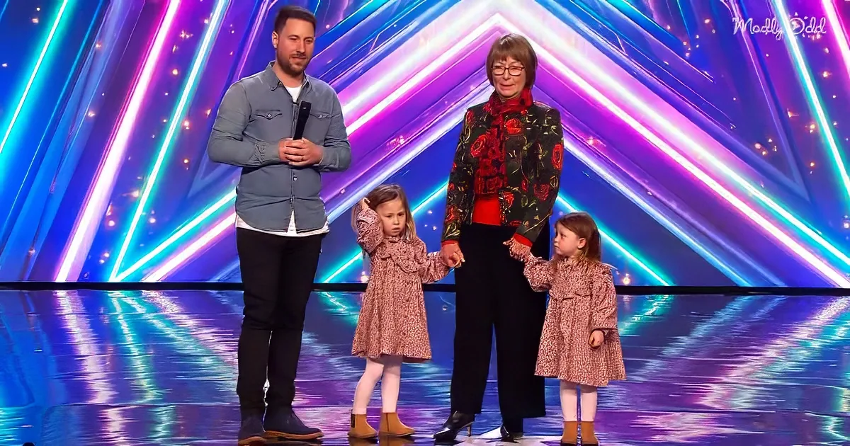 A man, woman, and two young girls stand on a stage with colorful lights behind them.