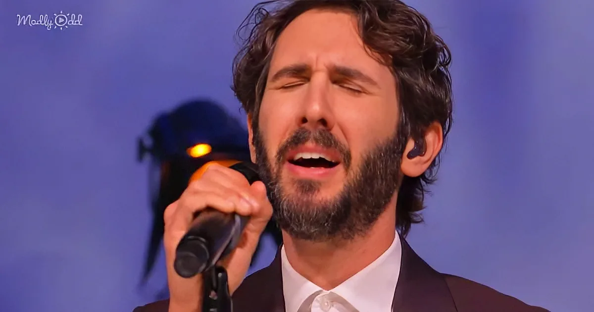 A man with a beard and curly hair sings passionately into a microphone, wearing a suit and tie.