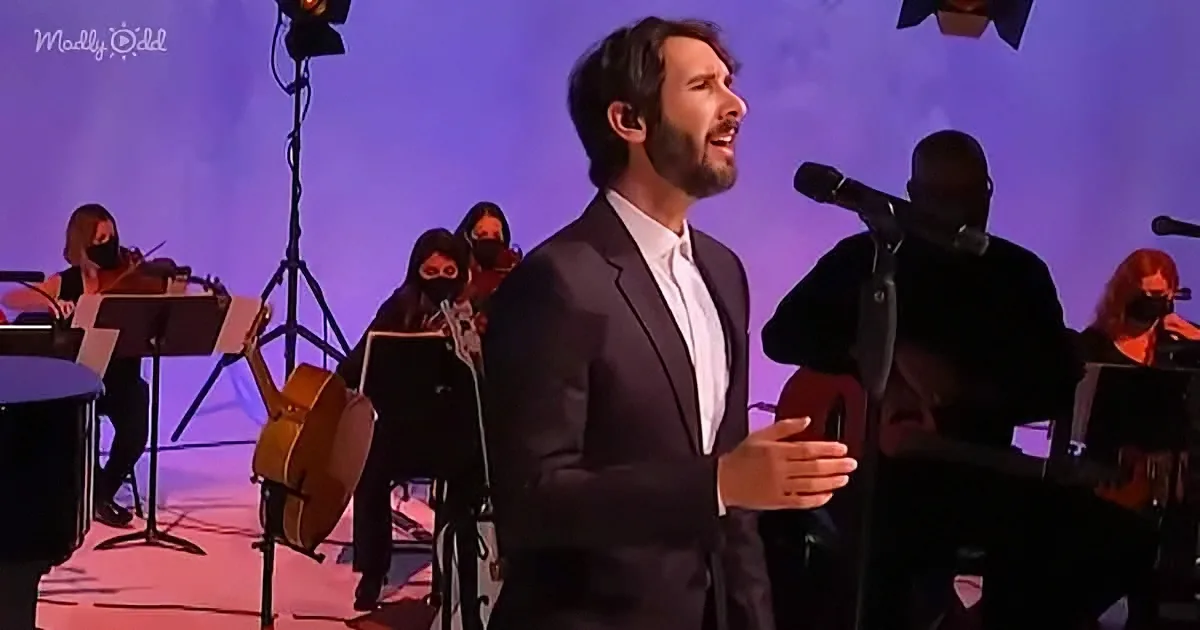 A man in a suit sings passionately on stage with an orchestra in the background.