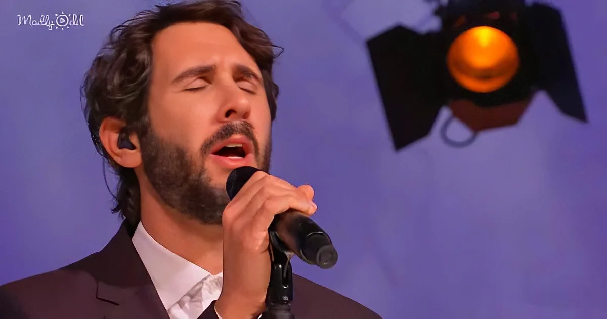 A man in a suit sings passionately into a microphone, eyes closed, against a purple backdrop with a spotlight.