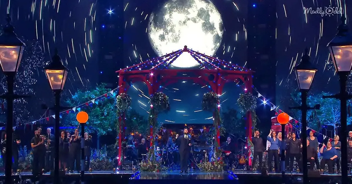 A large, bright moon dominates the night sky, casting a magical glow over a festive stage with a red gazebo and a crowd...