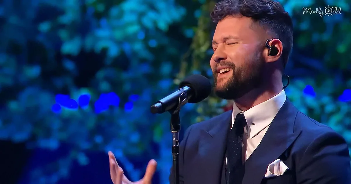 A man in a suit sings into a microphone, gesturing with his hand, against a blue-lit background.