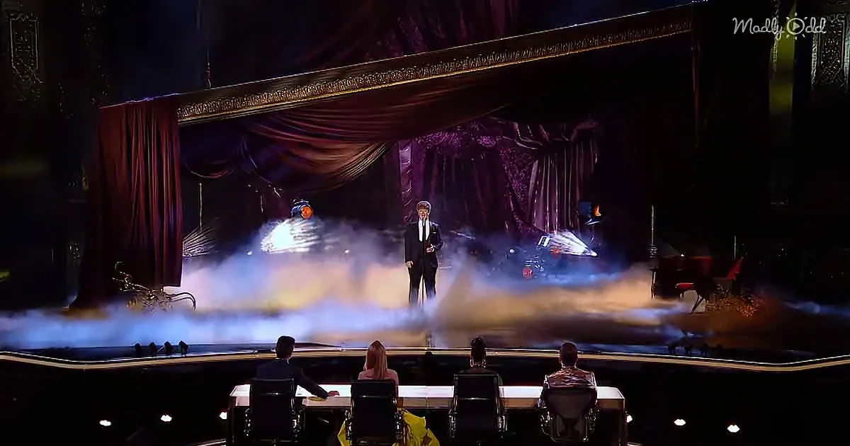 A man in a suit stands on a stage with smoke, surrounded by judges at a table.