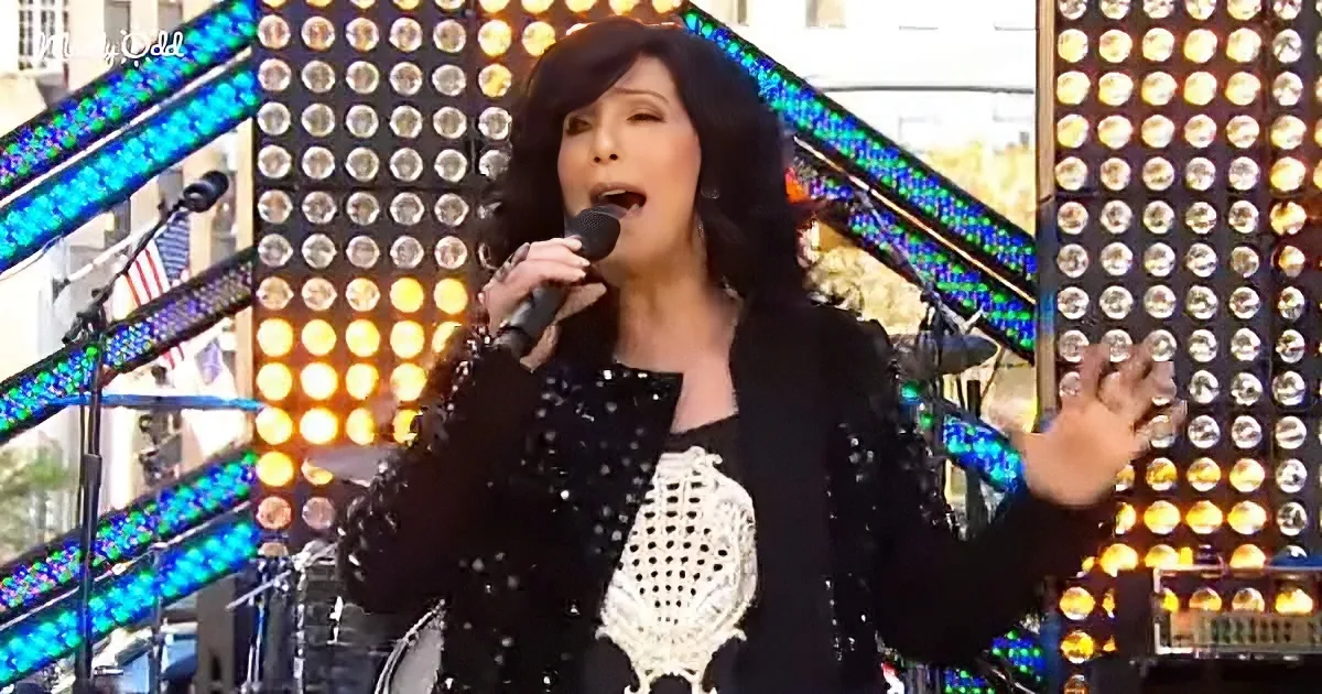 A woman in a black sequined outfit sings into a microphone on a stage with bright lights.