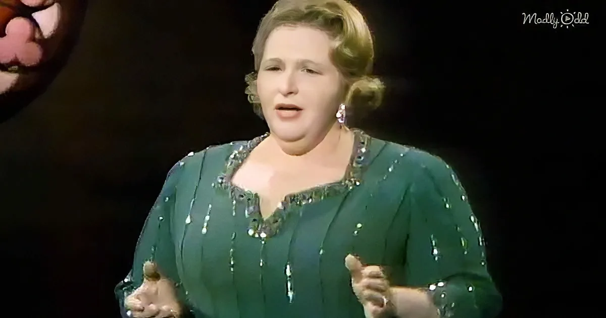 A woman in a green sequined dress sings on stage, her hands raised.