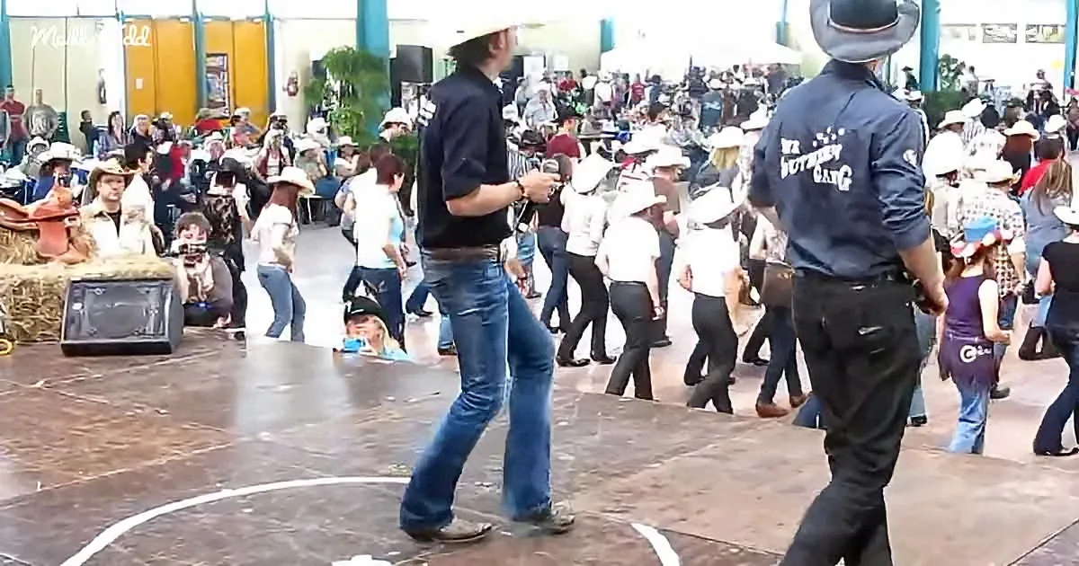 A man in a cowboy hat dances on a stage surrounded by a crowd at a lively event.
