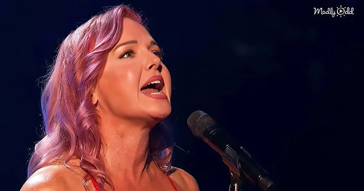 A woman with pink hair sings into a microphone, her eyes closed, against a dark background.
