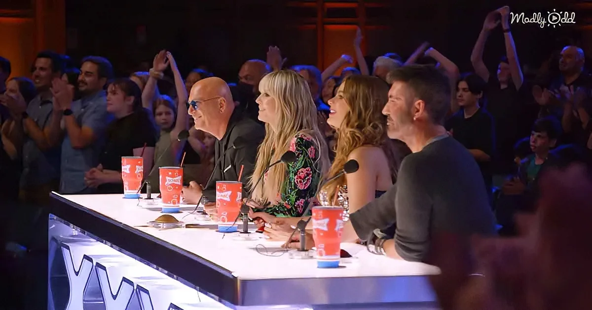 Judges at a table with microphones and audience in the background cheering.