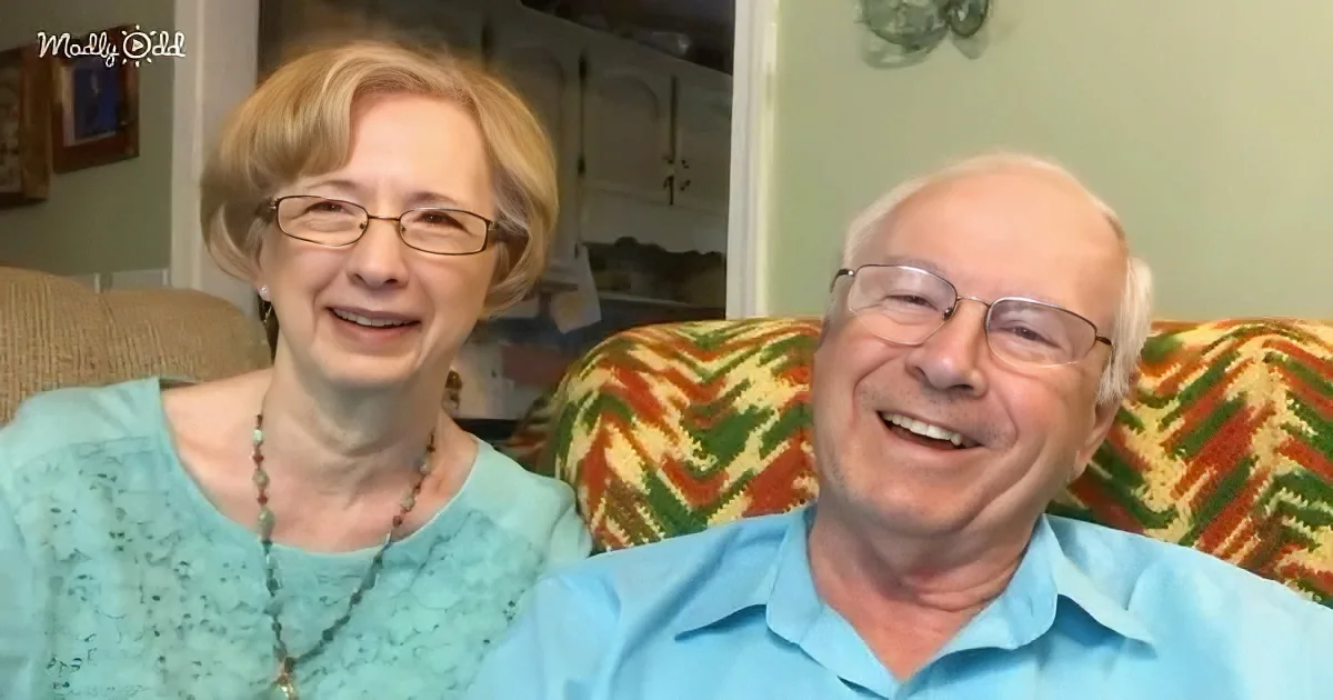 An older couple sits together on a colorful couch, both smiling warmly.
