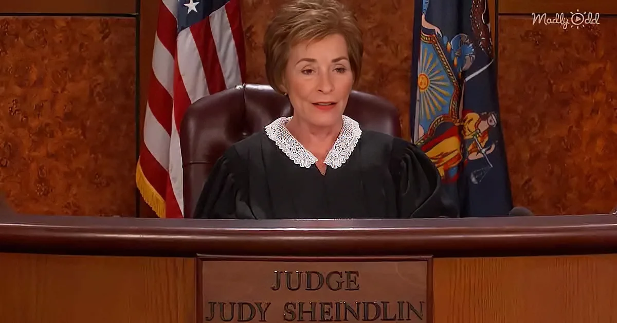 Judge Judy Sheindlin sits at her bench with an American flag and state flag behind her.