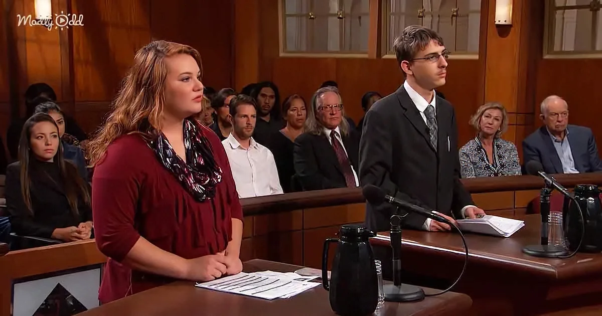 A woman in a red blouse stands at a podium, facing a man in a suit in a courtroom setting.