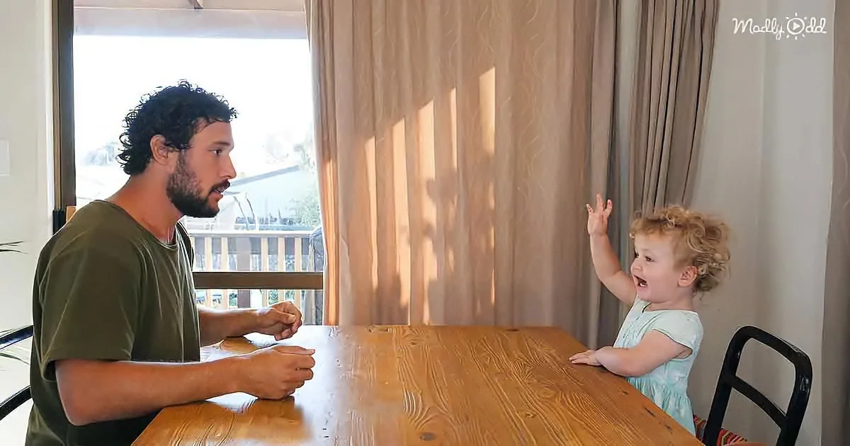 A man and a young child are seated at a wooden table, engaged in a conversation in a well-lit room.