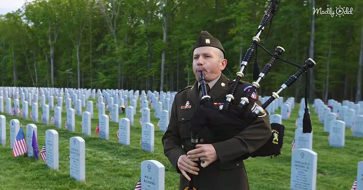 A man in military uniform plays bagpipes in a cemetery with rows of headstones.